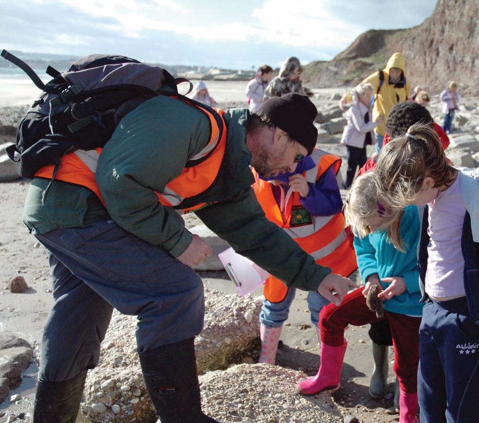 Fossil walk , group of children examining a fossil with museum expert
